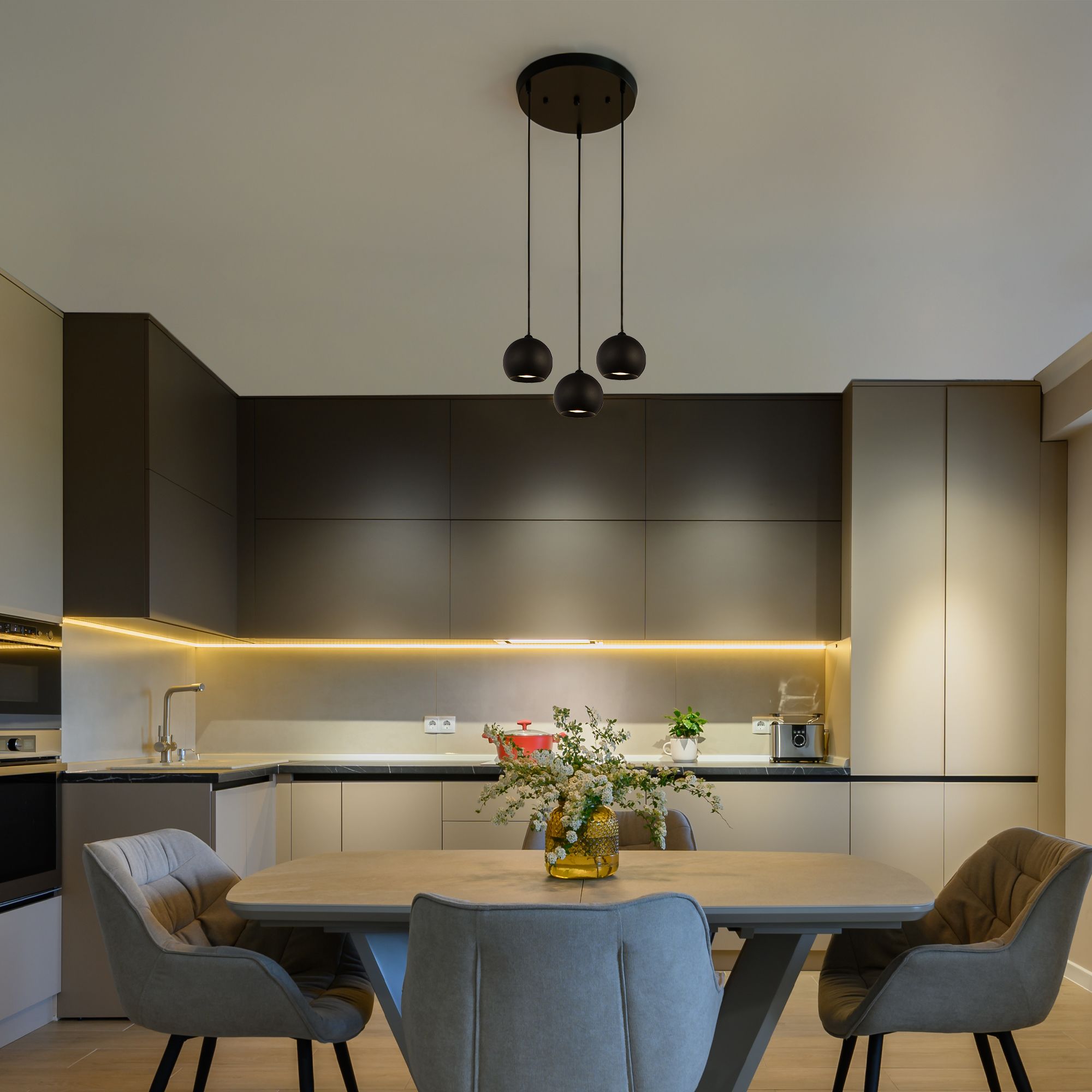 Searchlight Eindhoven 3 Light Pendant in sand black hanging above a dining table in a kitchen diner with wood cabinetry and a vase of flowers