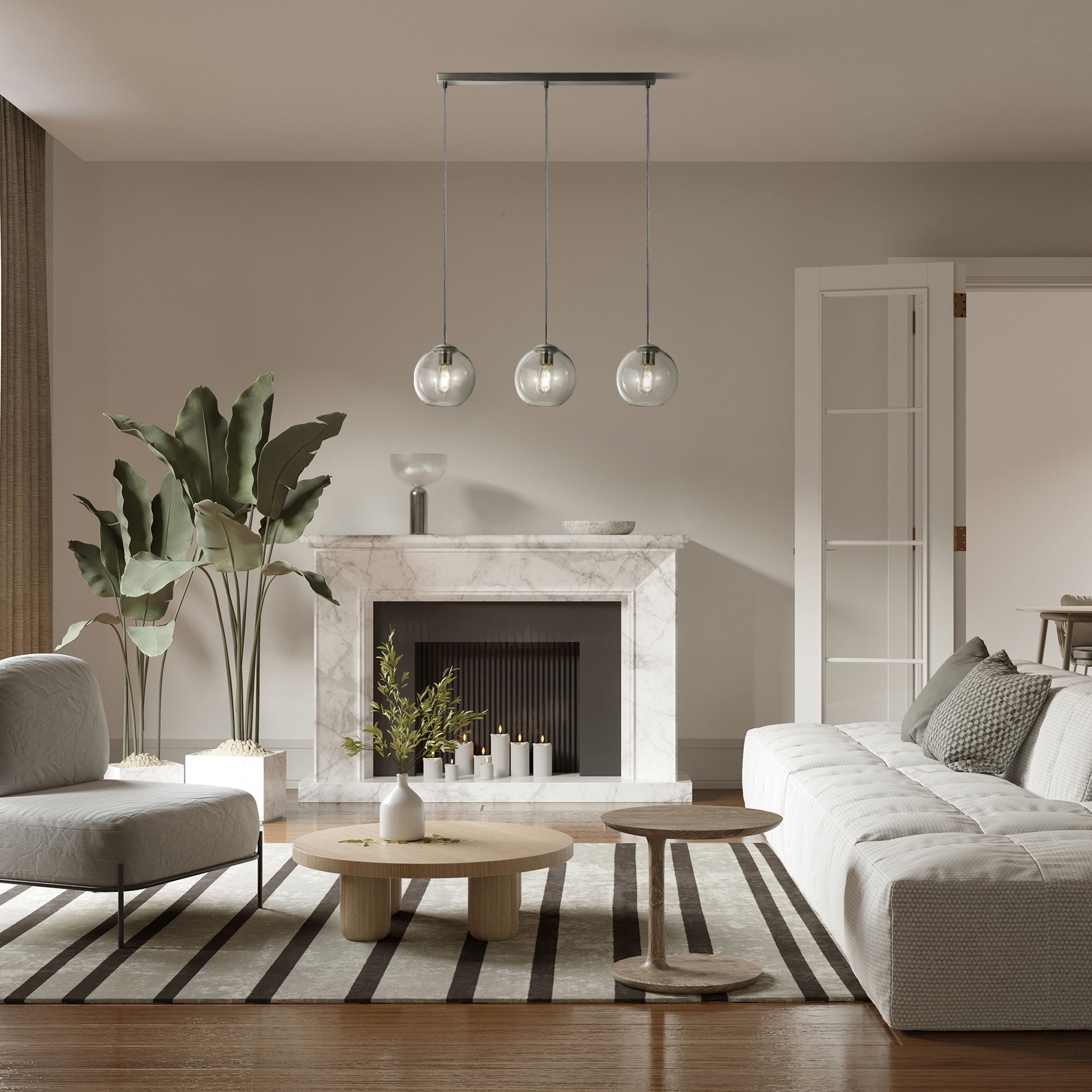Searchlight Balls 3 Light Bar Pendant in chrome and clear glass styled above a coffee table in a neutral living room with a marble fireplace