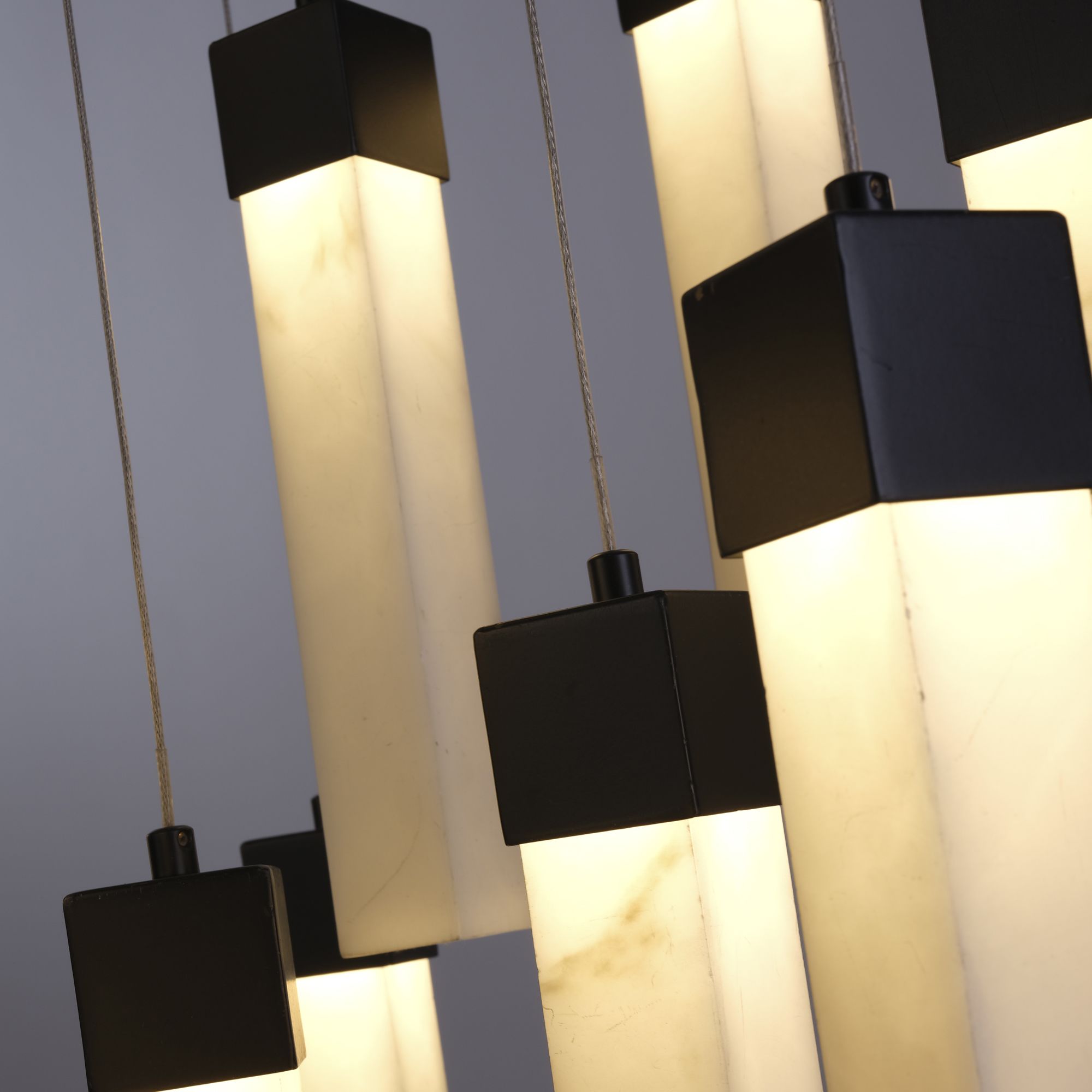 Close up of several marbleised resin bars and black end caps on the Searchlight Moonbeam 13 Light Pendant, lit from within