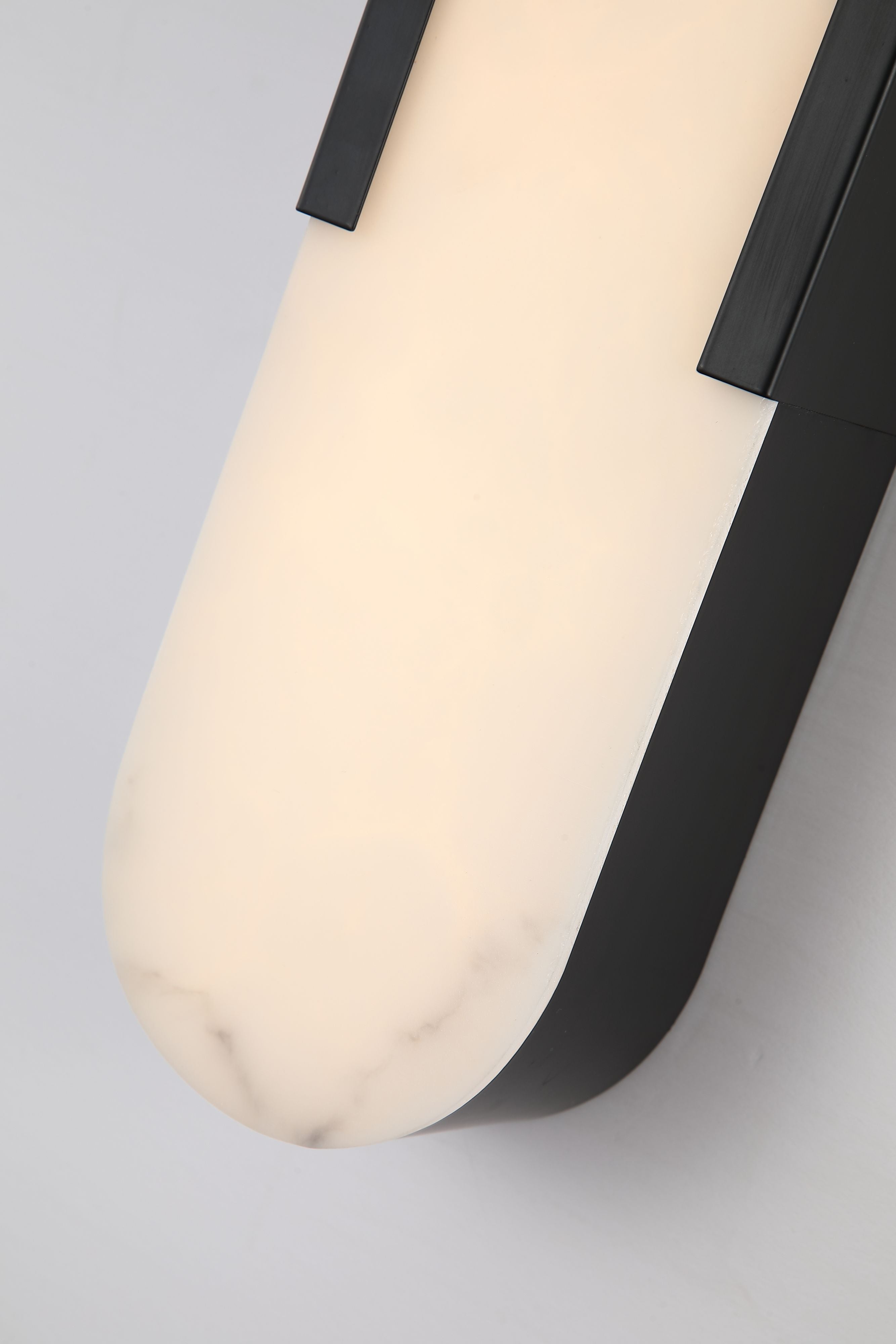 Close up of the Opaline wall light's rounded top edge, showing the marble veining in the resin panel against the matt black frame