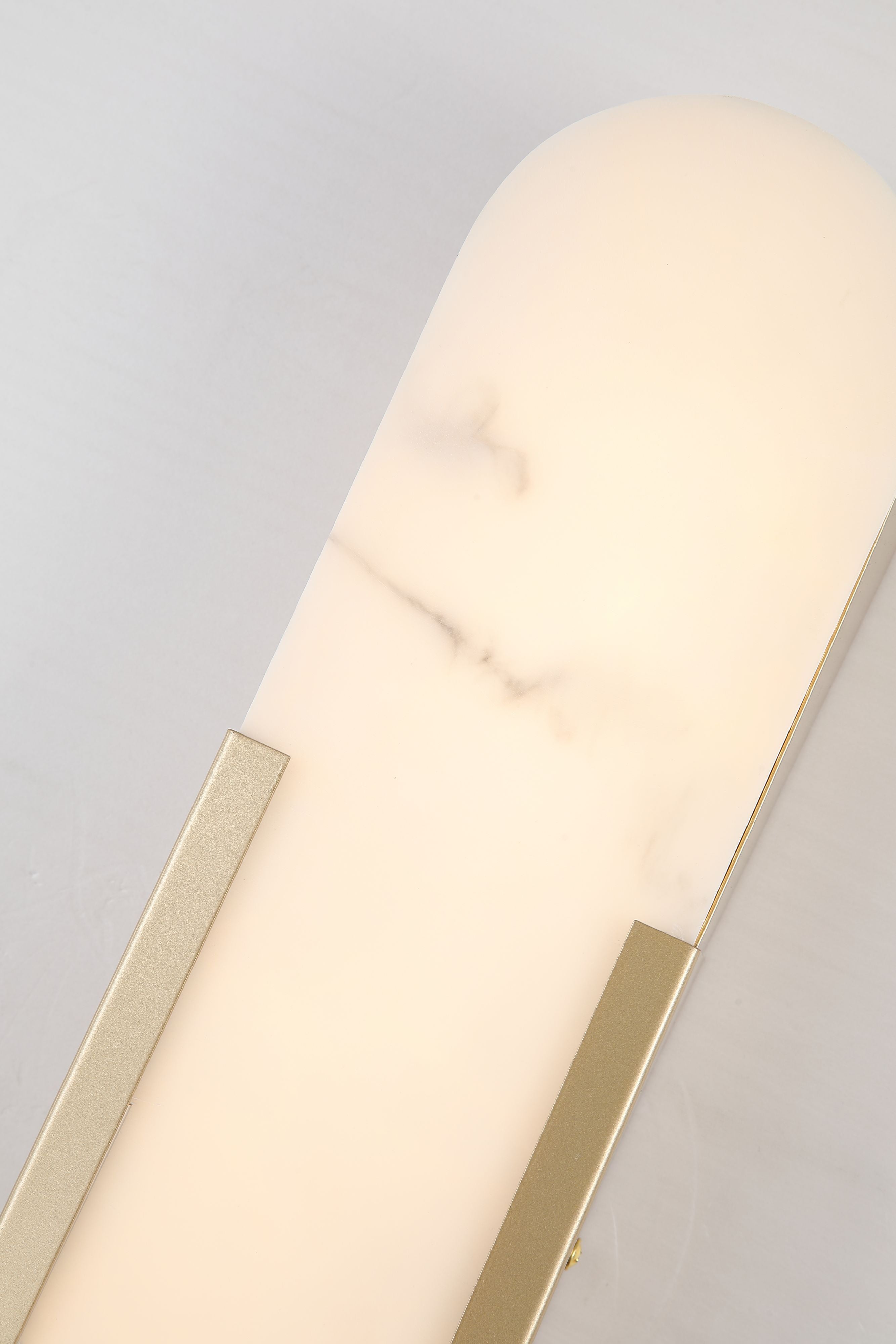 Close up of the gold Opaline wall light's top edge, showing marble veining in the resin panel against the brushed gold frame