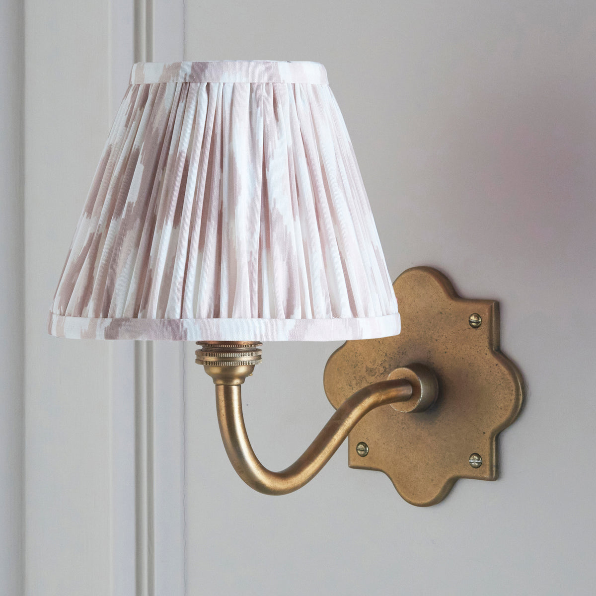 Endon Anvil Curve wall light switched off on a grey panelled wall, showing the antique brass backplate, curved arm and neutral ikat shade