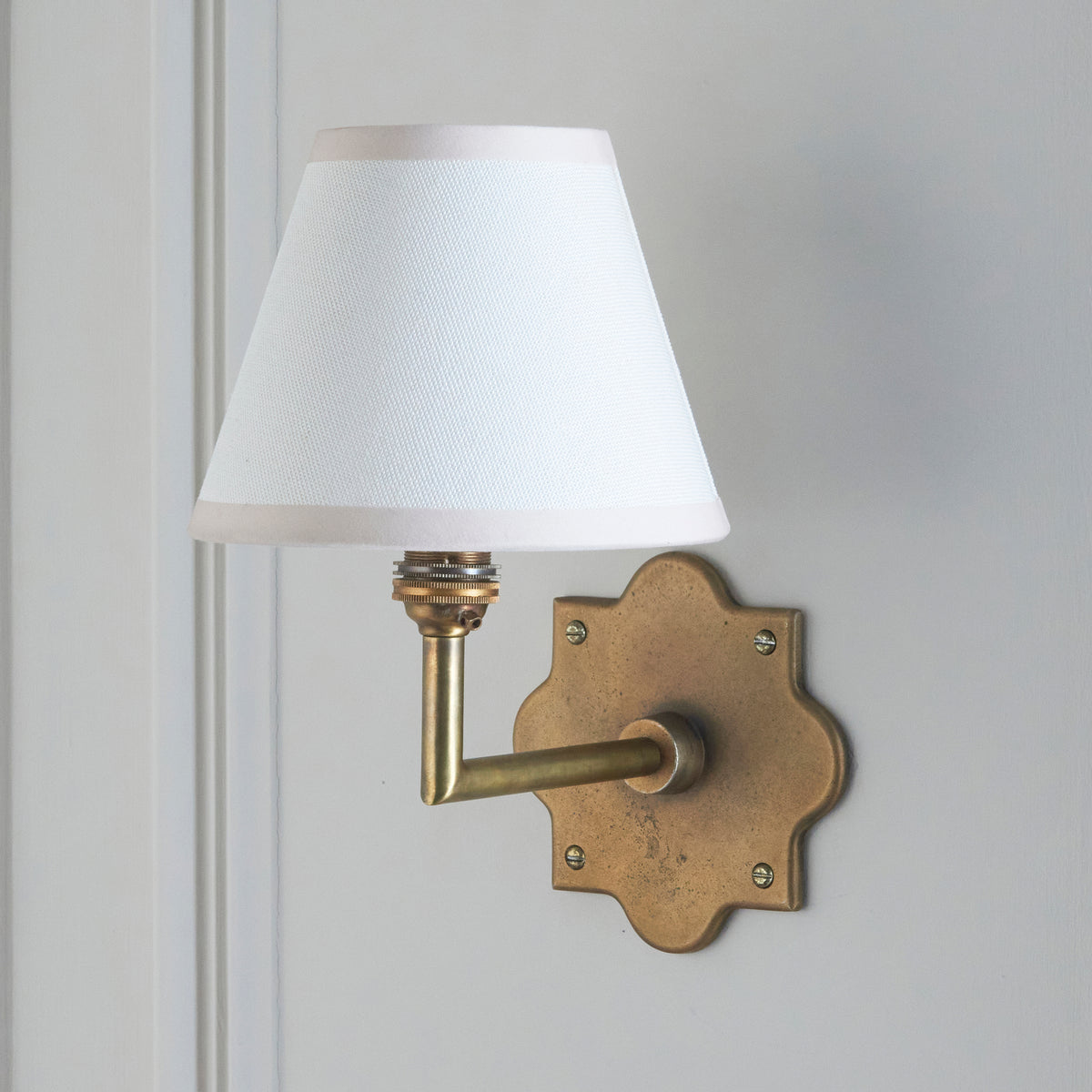 Endon Anvil Angle wall light unlit on a pale grey panelled wall, antique brass backplate to the right of the vintage white shade