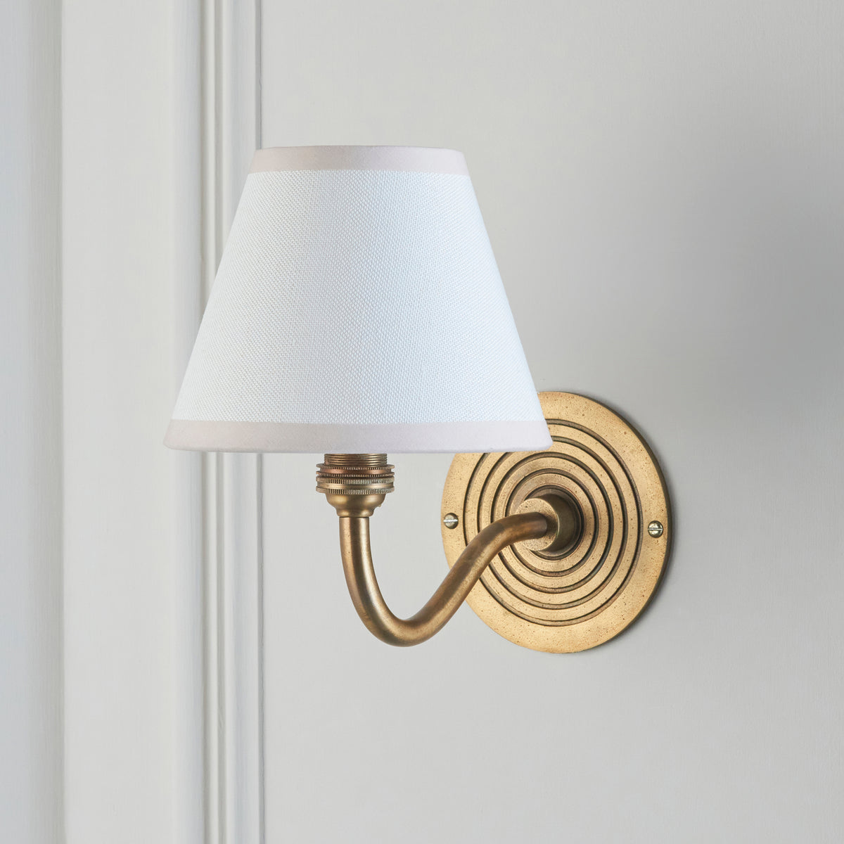 Endon Ripple Curve antique brass wall light with vintage white shade, unlit, mounted on a pale grey panelled wall