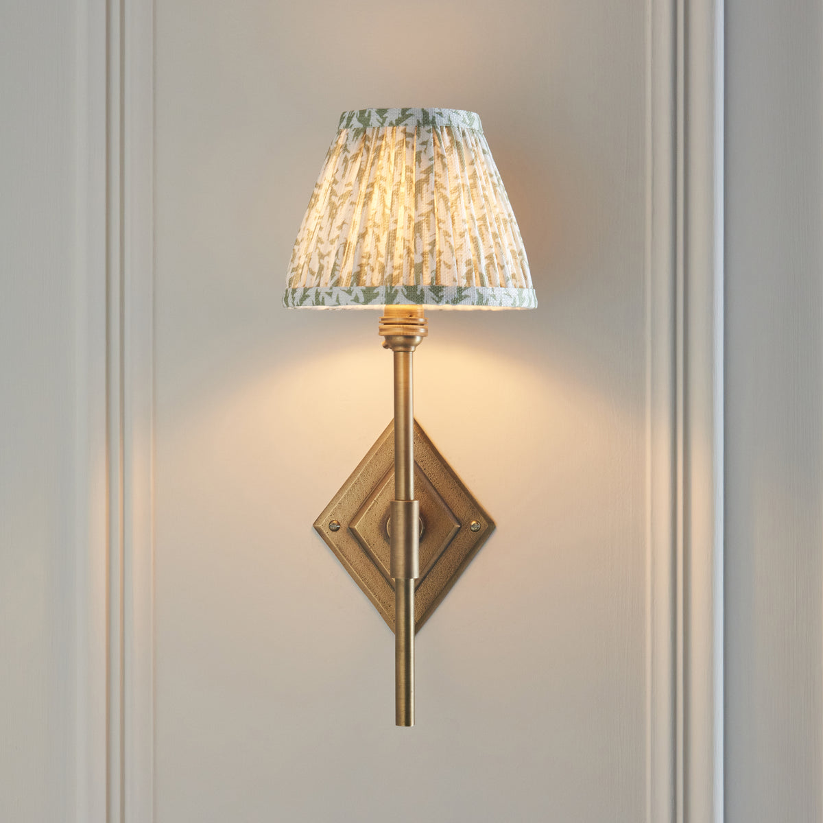 Lit Endon Diamond Tall wall light showing the full diamond antique brass backplate and green leaf print shade on cream panelling