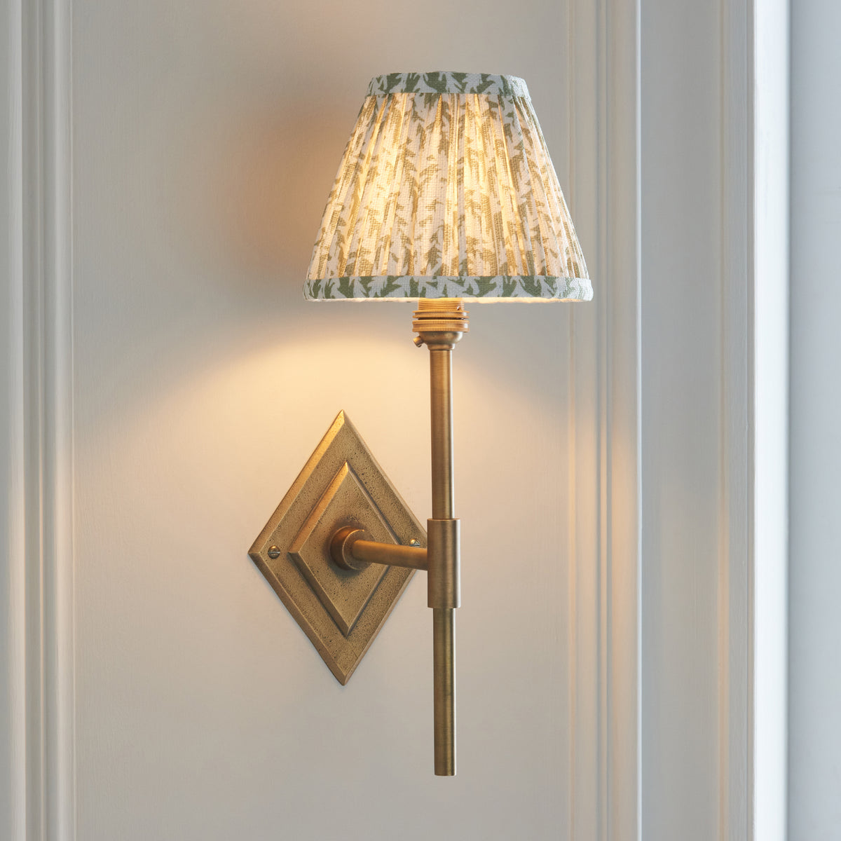 Endon Diamond Tall brass wall light with herb garden green leaf shade glowing on a panelled wall beside a window