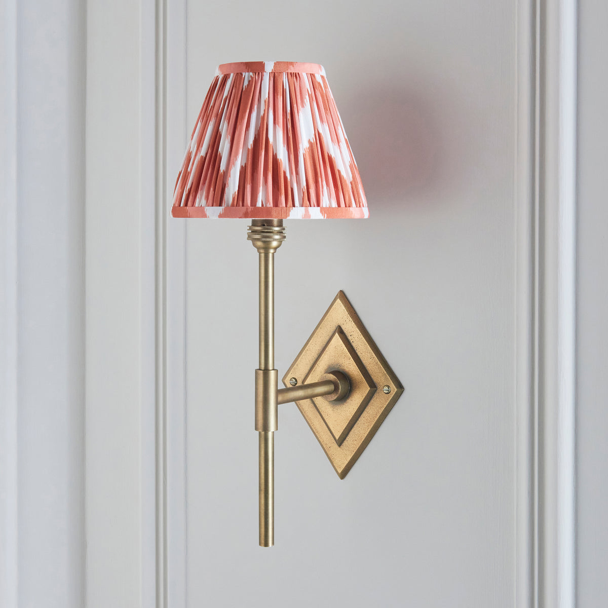 Endon Diamond Tall wall light switched off on a pale grey panelled wall, antique brass diamond backplate with apricot orange zigzag pleated shade