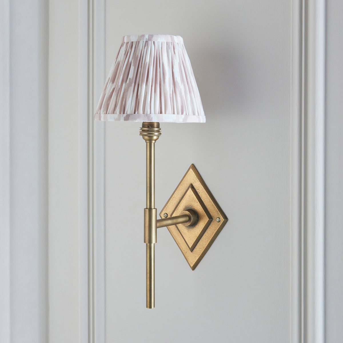 Endon Diamond Tall wall light unlit on a pale panelled wall, antique brass diamond backplate and stem with a pink and white ikat shade