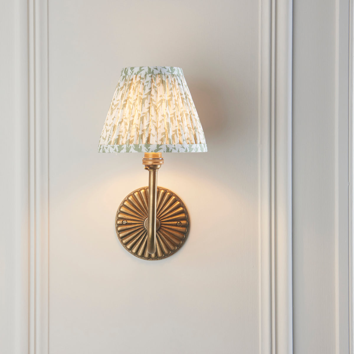 Endon Dahlia Swan wall light lit on a cream panelled wall, the swan neck arm appearing straight in front of the fluted antique brass backplate