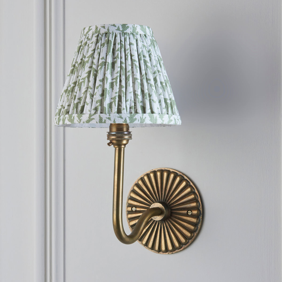 Endon Dahlia Swan antique brass wall light with 16cm green leaf pleated shade, switched off, on a pale grey panelled wall