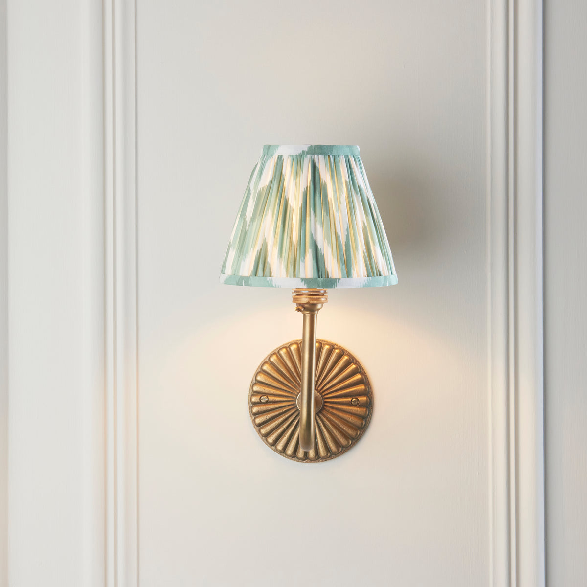Endon Dahlia Swan wall light lit on cream panelling, swan neck arm hidden behind the green zigzag shade, fluted brass backplate below