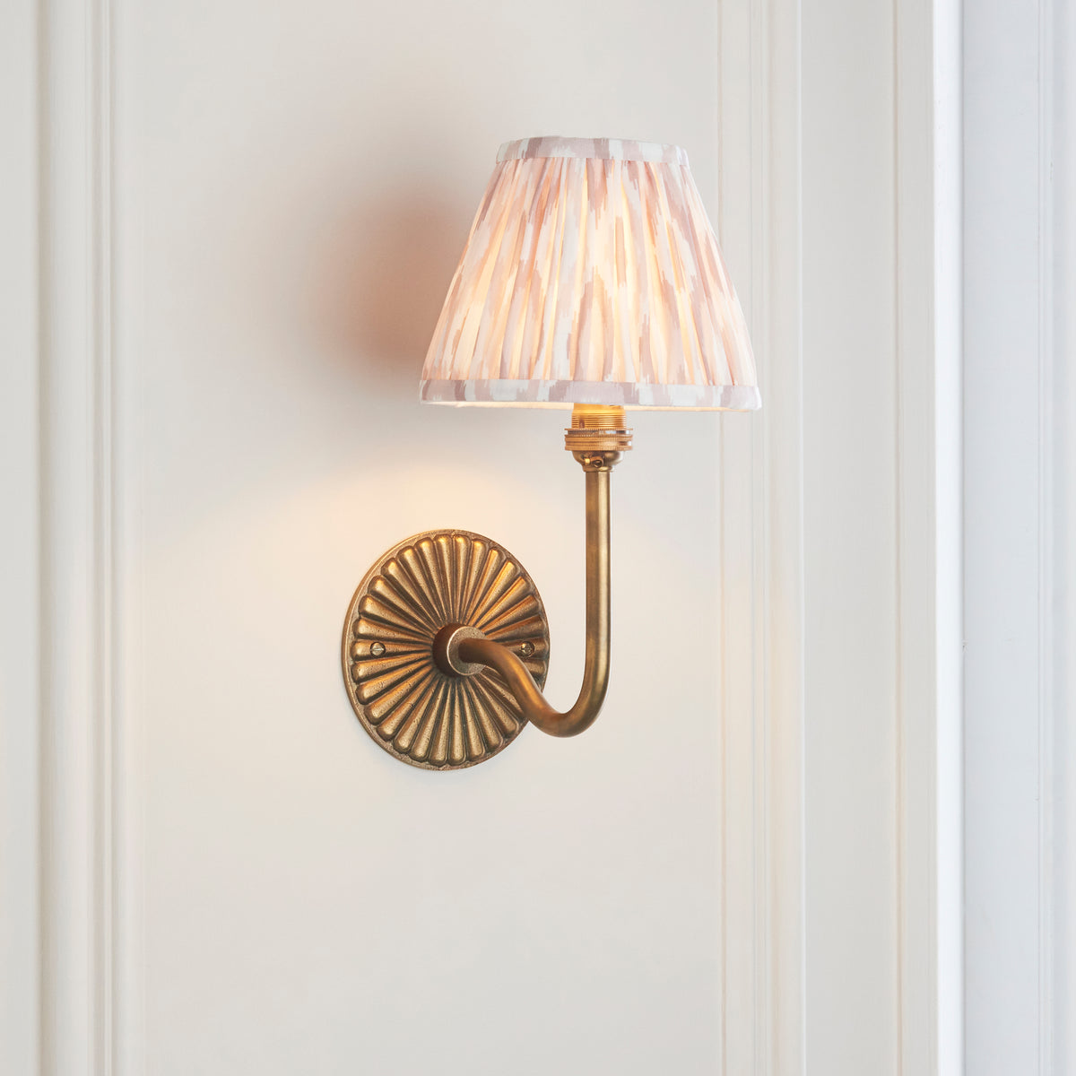 Endon Dahlia Swan antique brass wall light lit in a cream panelled room with a door frame to one side