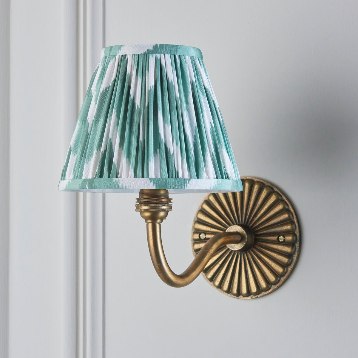 Endon Dahlia Curve antique brass wall light switched off on a grey panelled wall, showing the crisp green and white zigzag print