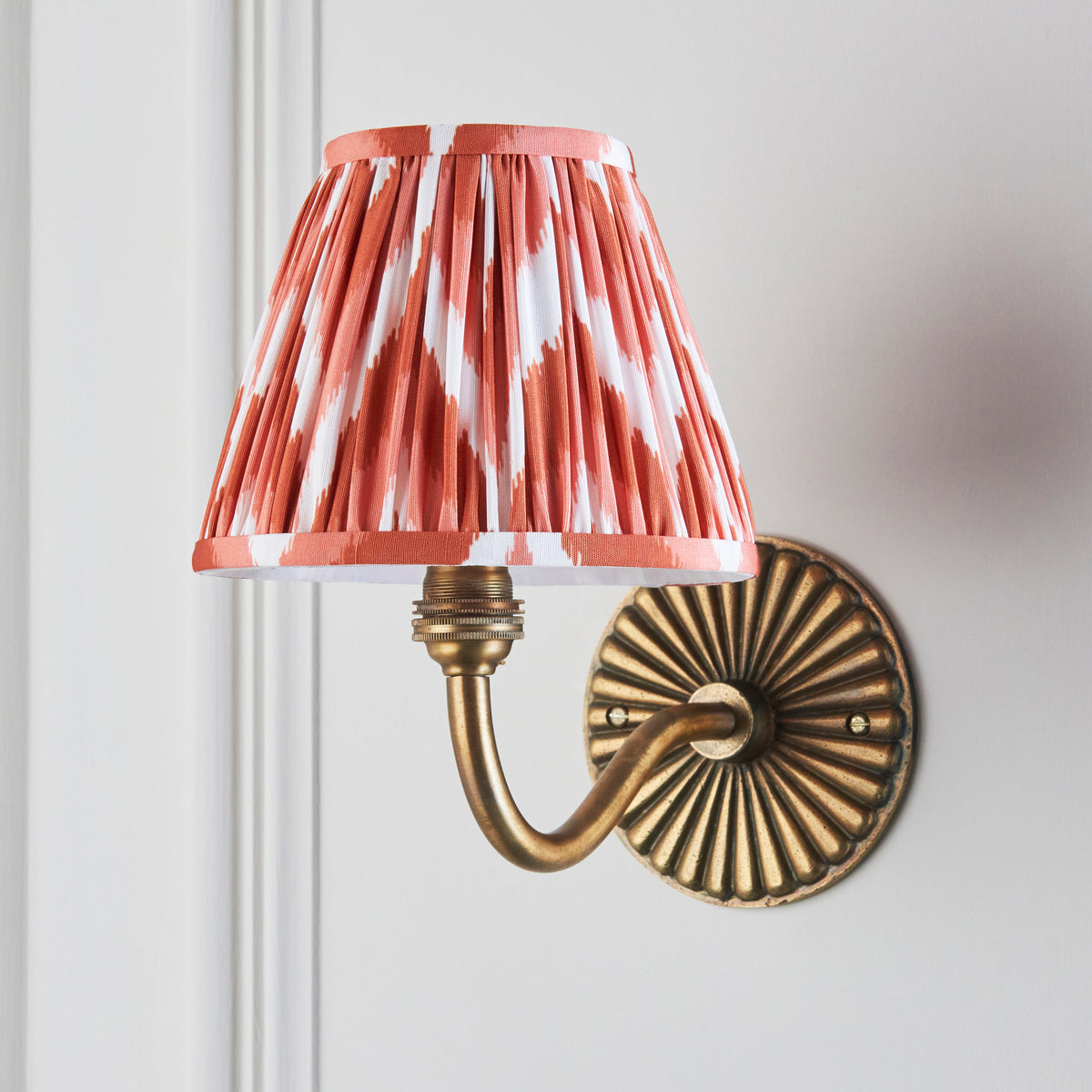 Endon Dahlia Curve antique brass wall light unlit on a cream panelled wall with apricot orange zigzag pleated shade