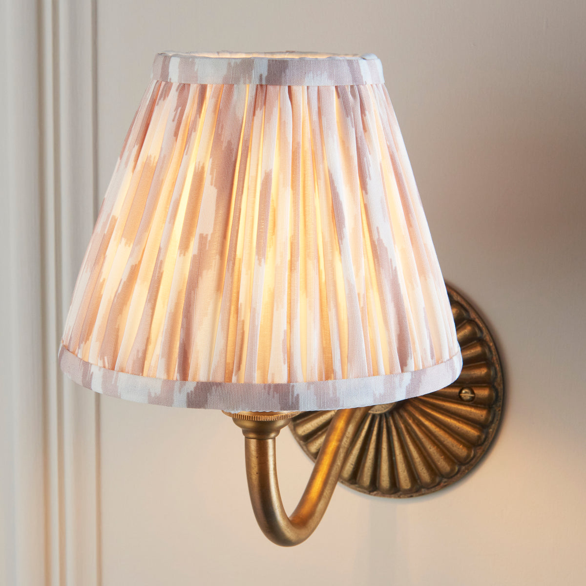 Close up of the lit neutral ikat pleated shade on the Endon Dahlia Curve antique brass wall light