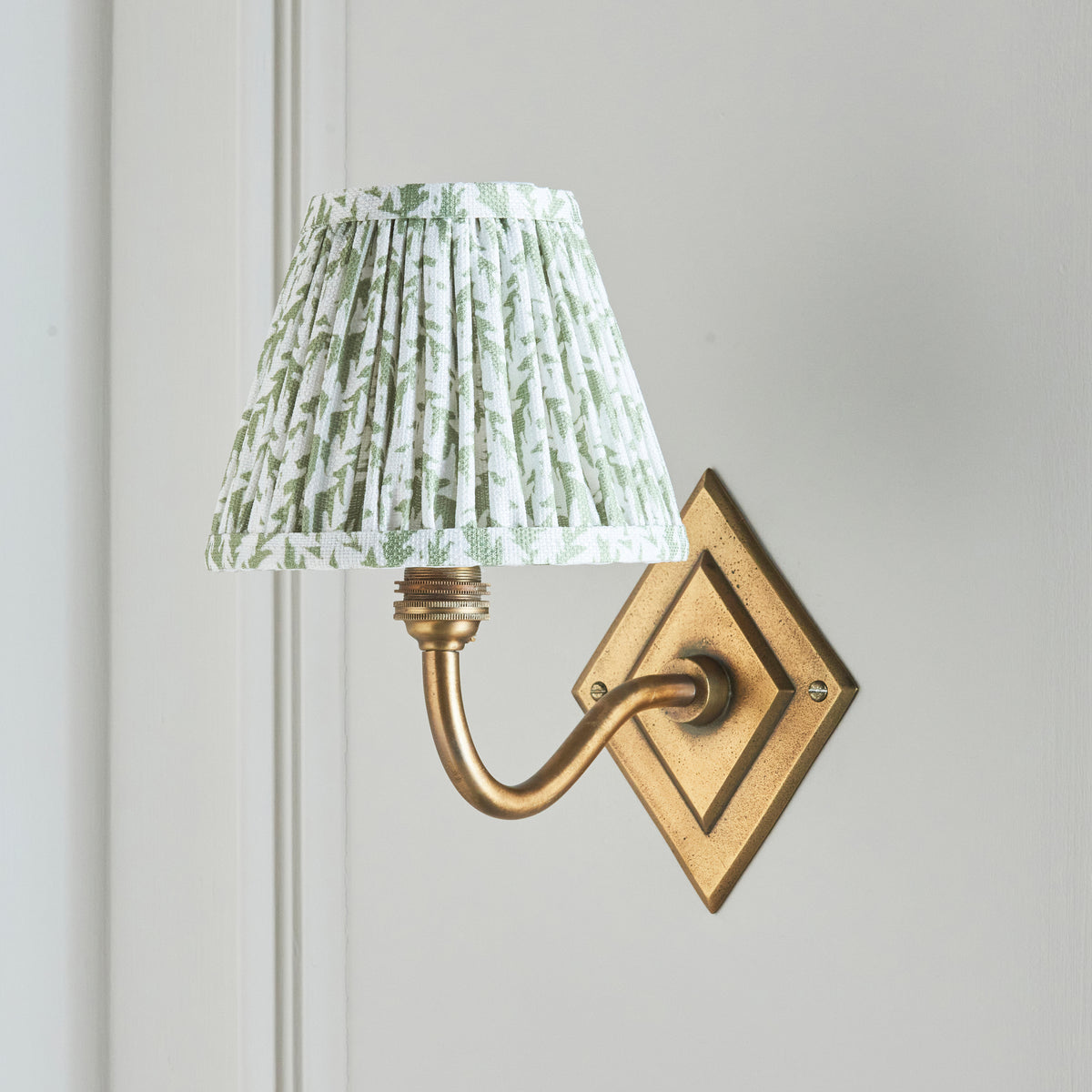 Unlit Endon Diamond Curve wall light on a cream panelled wall showing the antique brass backplate, curved arm and green leaf shade