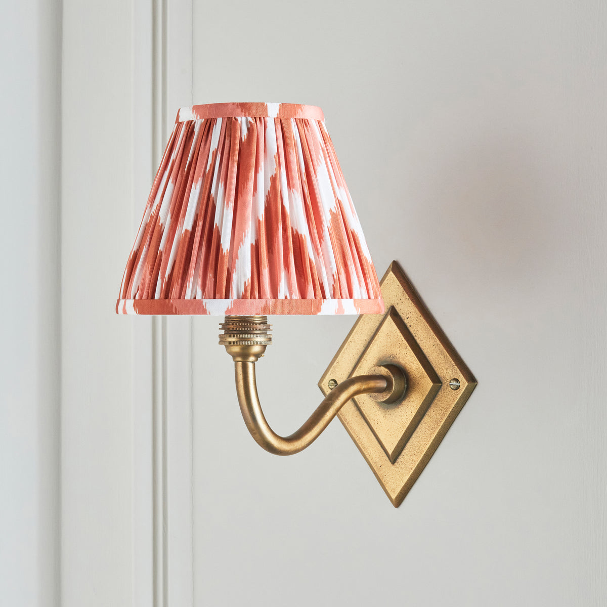 Endon Diamond Curve wall light switched off on a cream panelled wall, antique brass diamond backplate and apricot orange zigzag shade