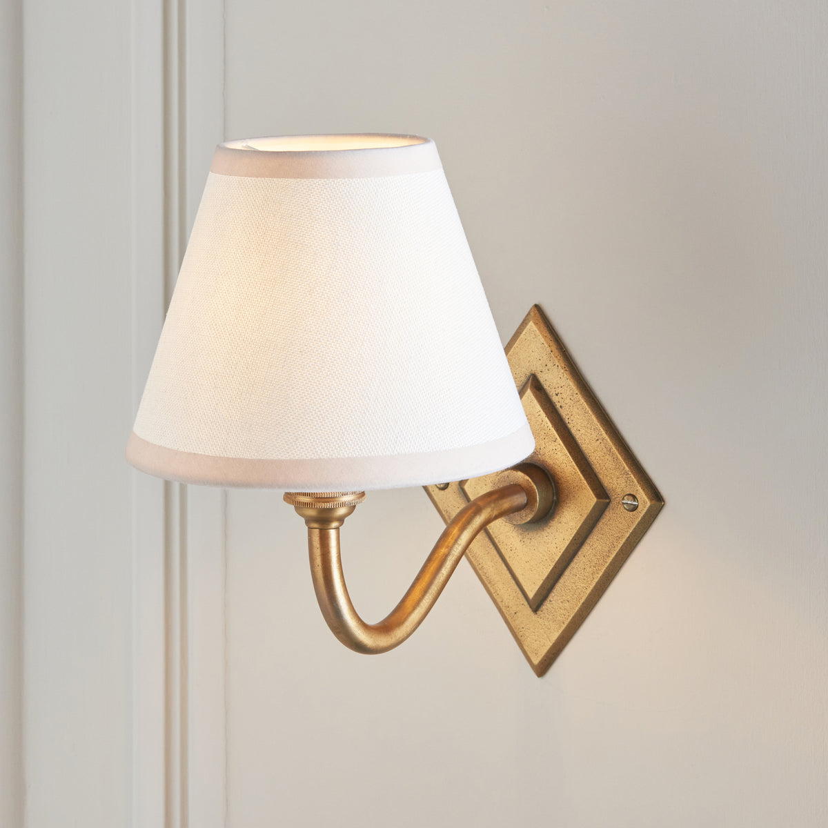 Endon Diamond Curve wall light unlit on a cream panelled wall, antique brass diamond backplate and vintage white taped edge shade