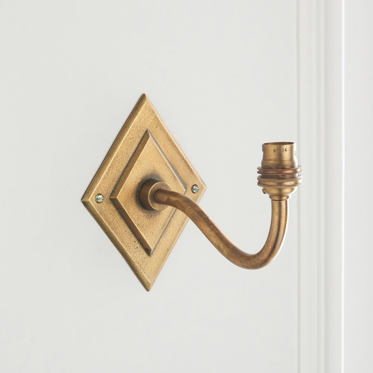 Endon Diamond Curve wall bracket without its shade, antique brass diamond backplate, curved arm and B22 lamp holder on a pale wall