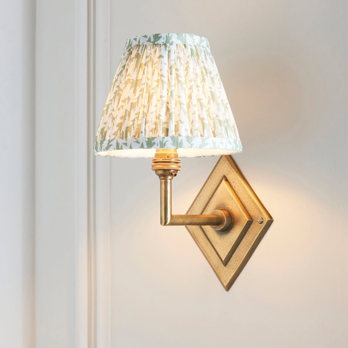 Endon Diamond Angle antique brass wall light with green leaf shade switched on against a cream panelled wall