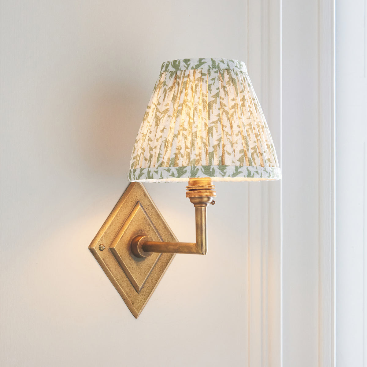 Endon Diamond Angle antique brass wall light glowing on a cream panelled wall beside a white window frame
