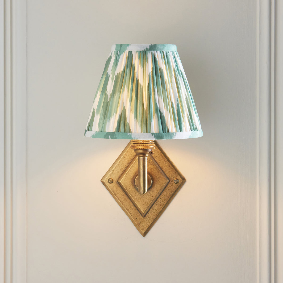 Endon Diamond Angle wall light lit on a cream panelled wall, green zigzag shade sitting directly above the antique brass diamond backplate