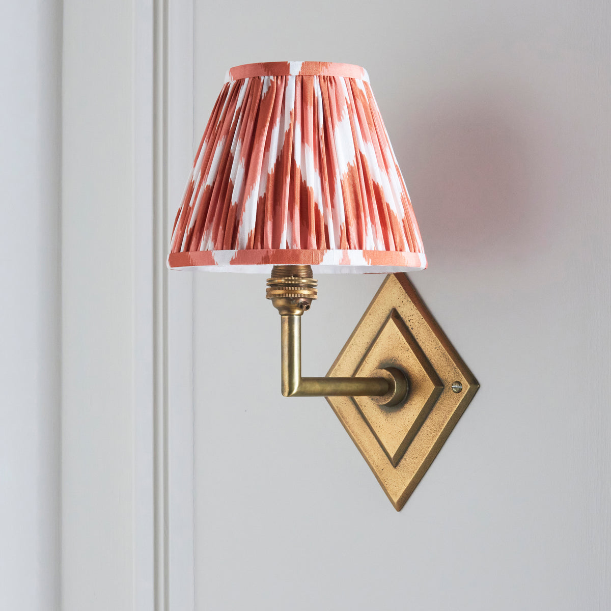Endon Diamond Angle wall light unlit on a cream panelled door, antique brass diamond backplate and apricot orange zigzag pleated shade