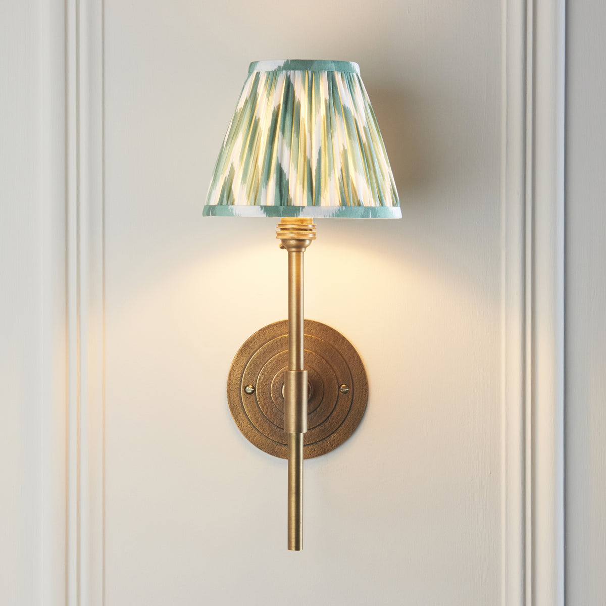 Lit Endon Halo Tall wall light with green zigzag shade on a cream panelled wall, stepped antique brass backplate centred behind the stem