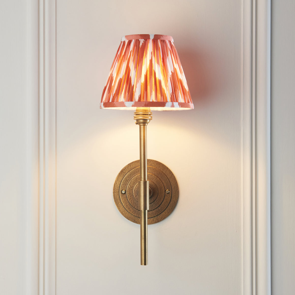 Lit Endon Halo Tall wall light with apricot orange zigzag shade casting a soft pool of light on a cream panelled wall
