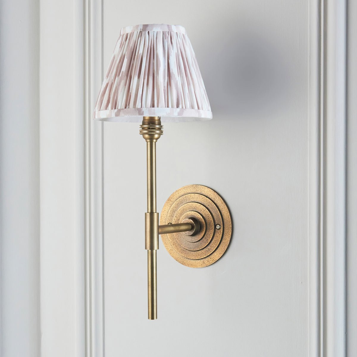 Endon Halo Tall wall light unlit on a pale grey panelled wall, antique brass backplate and stem with a pink and cream neutral Ikat shade