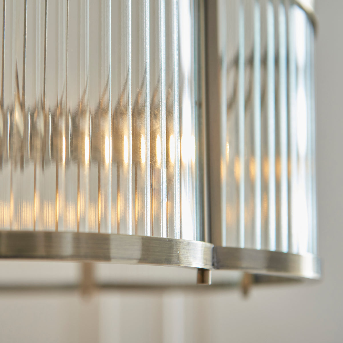 Extreme close up of the Ridgeton Scallop pendant's ribbed glass panels and frame edge, backlit with warm light.