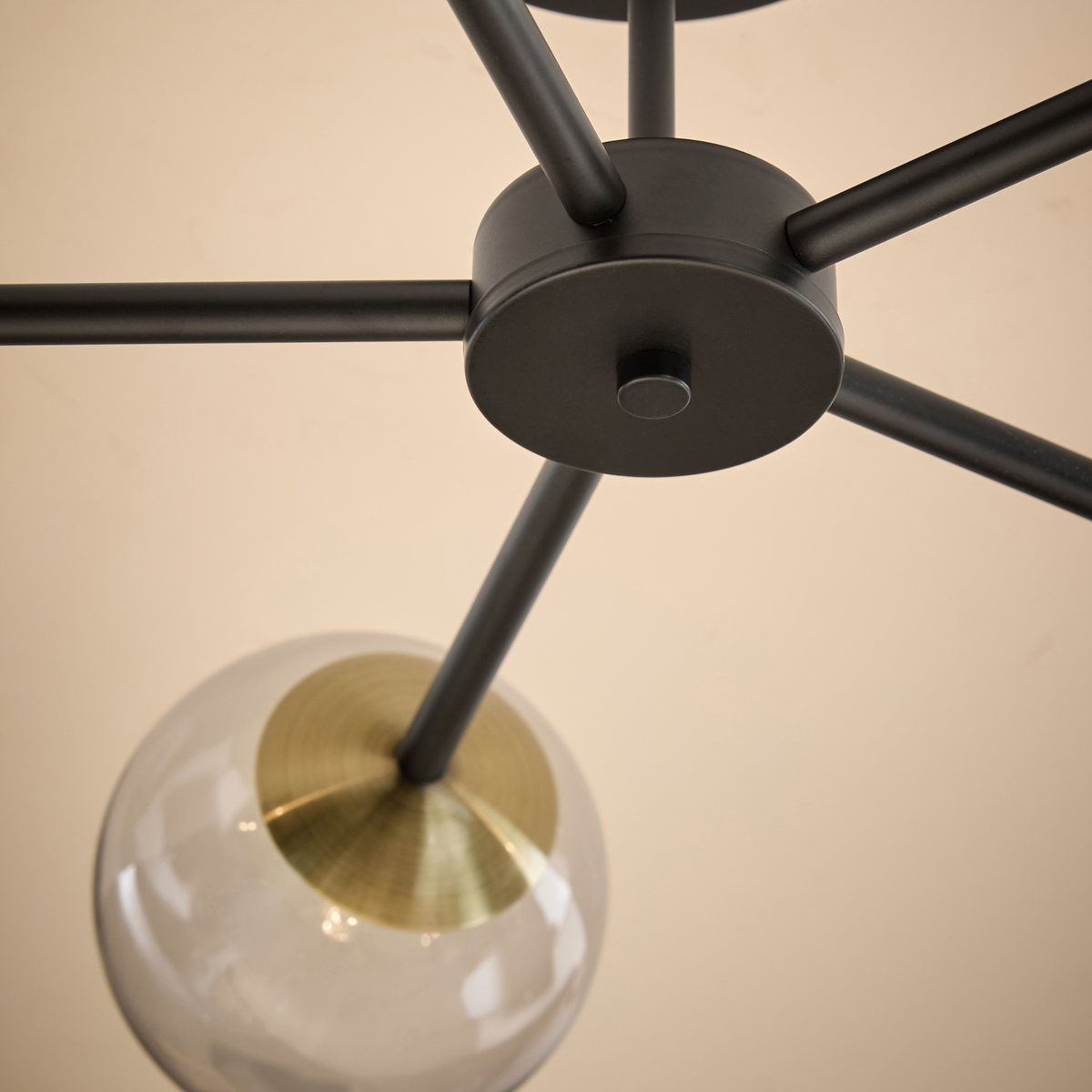 MADE.COM Globe 5 light flush ceiling light close up of matt black hub, arms and glass globe with brass detail