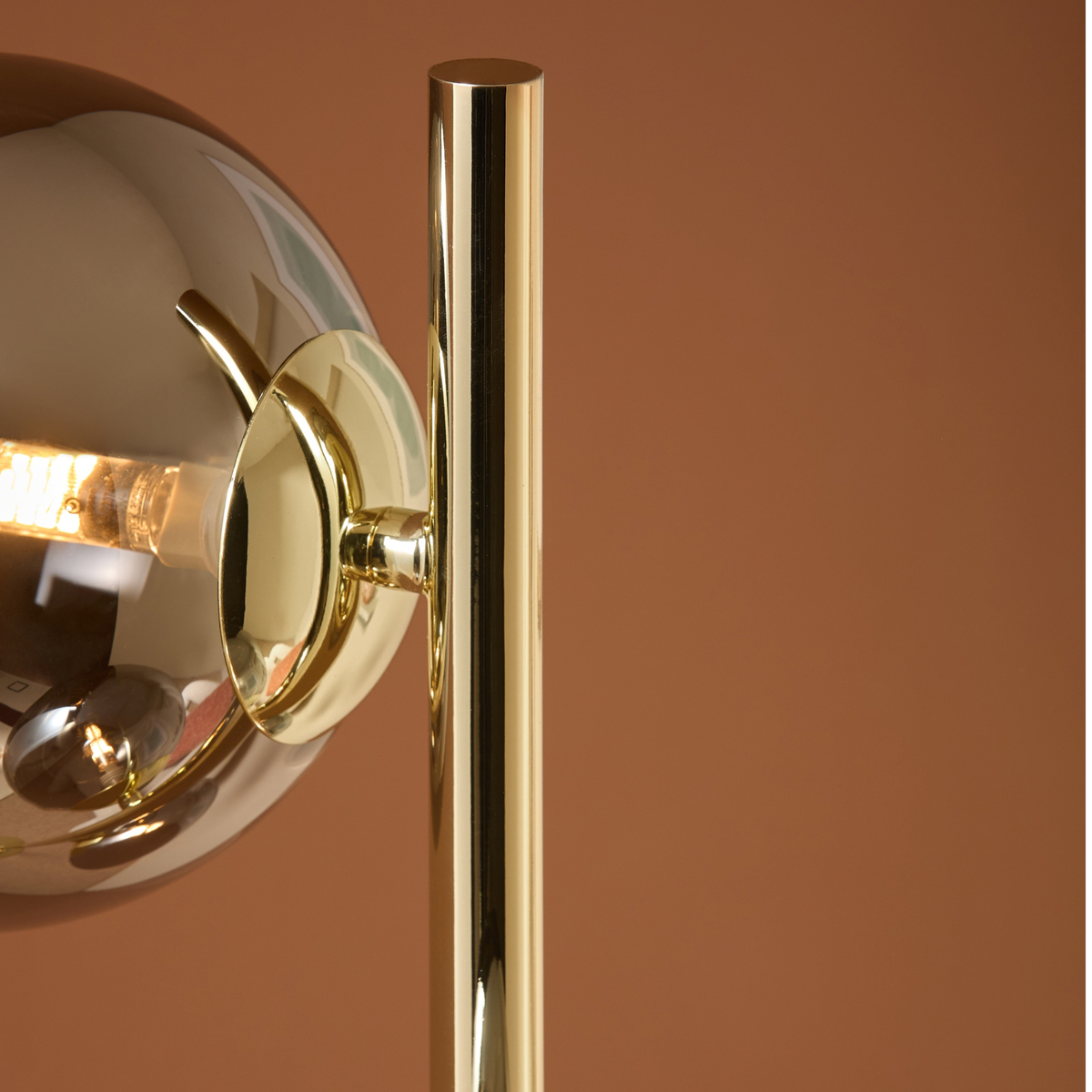 MADE Globe floor lamp close up of glass globe and polished brass pole against a terracotta wall