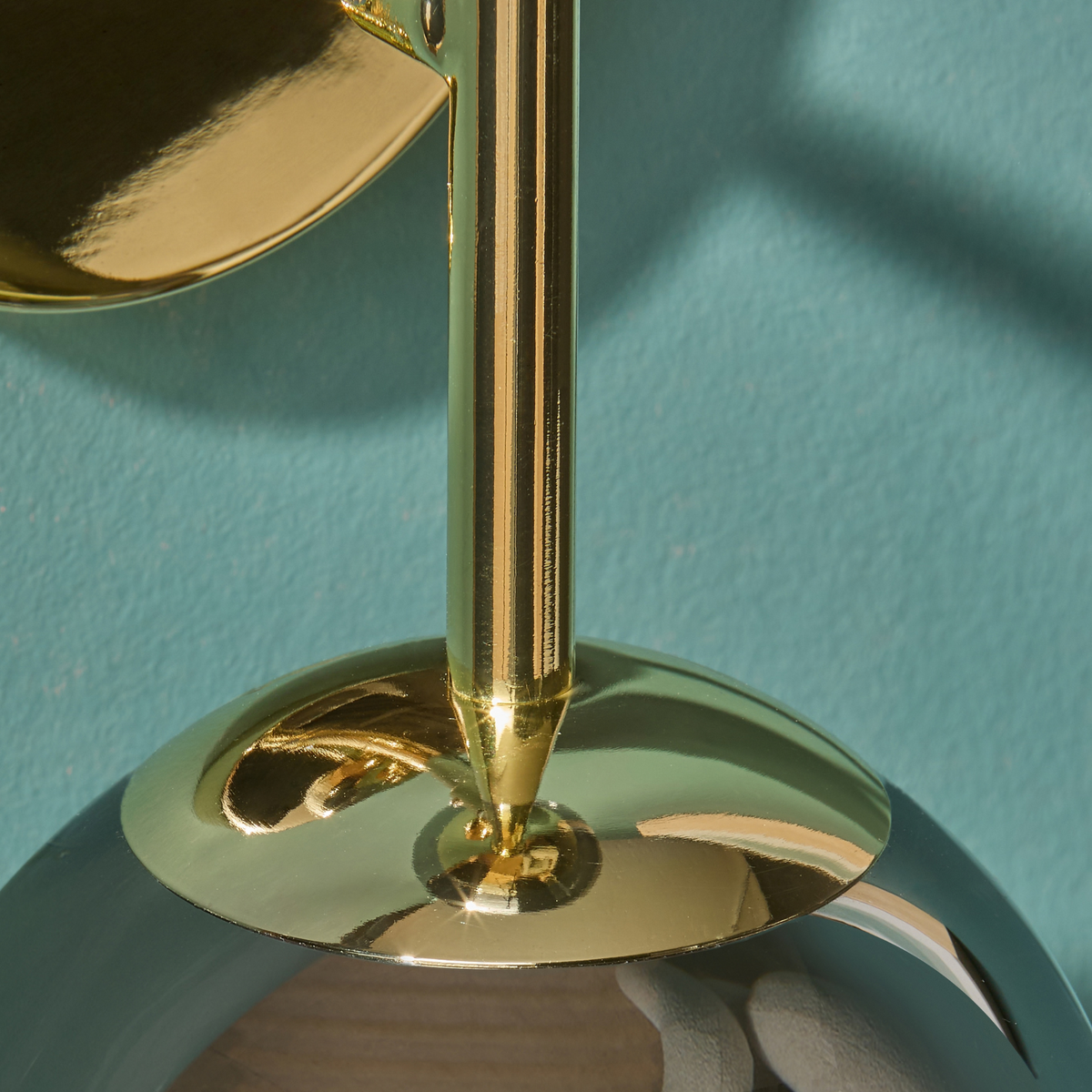 MADE Globe wall light close up of polished brass stem and glass globe cap on a teal wall