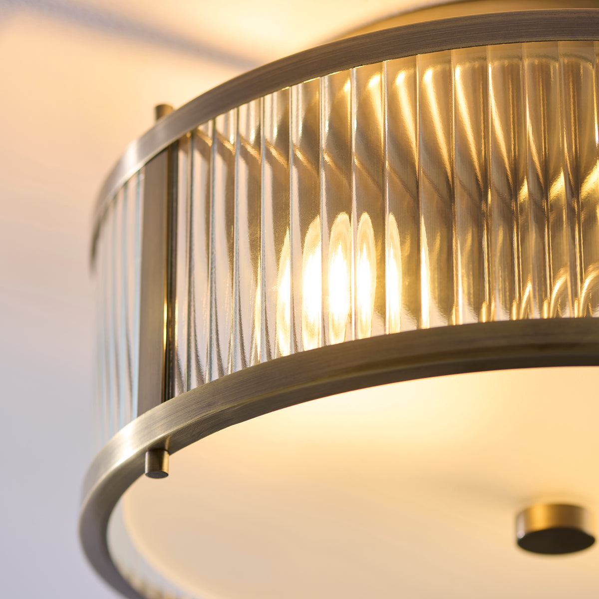 Extreme close up of the clear ribbed glass panels on the Endon Ridgeton IP44 flush ceiling light showing the antique brass frame and lit bulbs