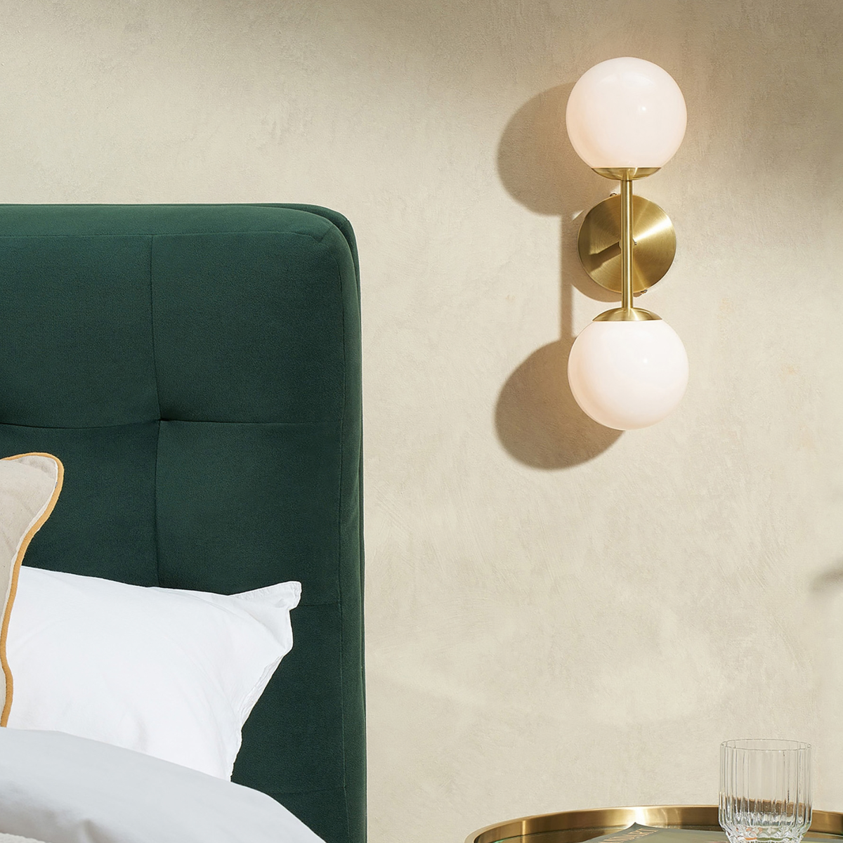MADE.COM Globe wall light in brushed brass with two opal glass globes, lifestyle shot beside a bed