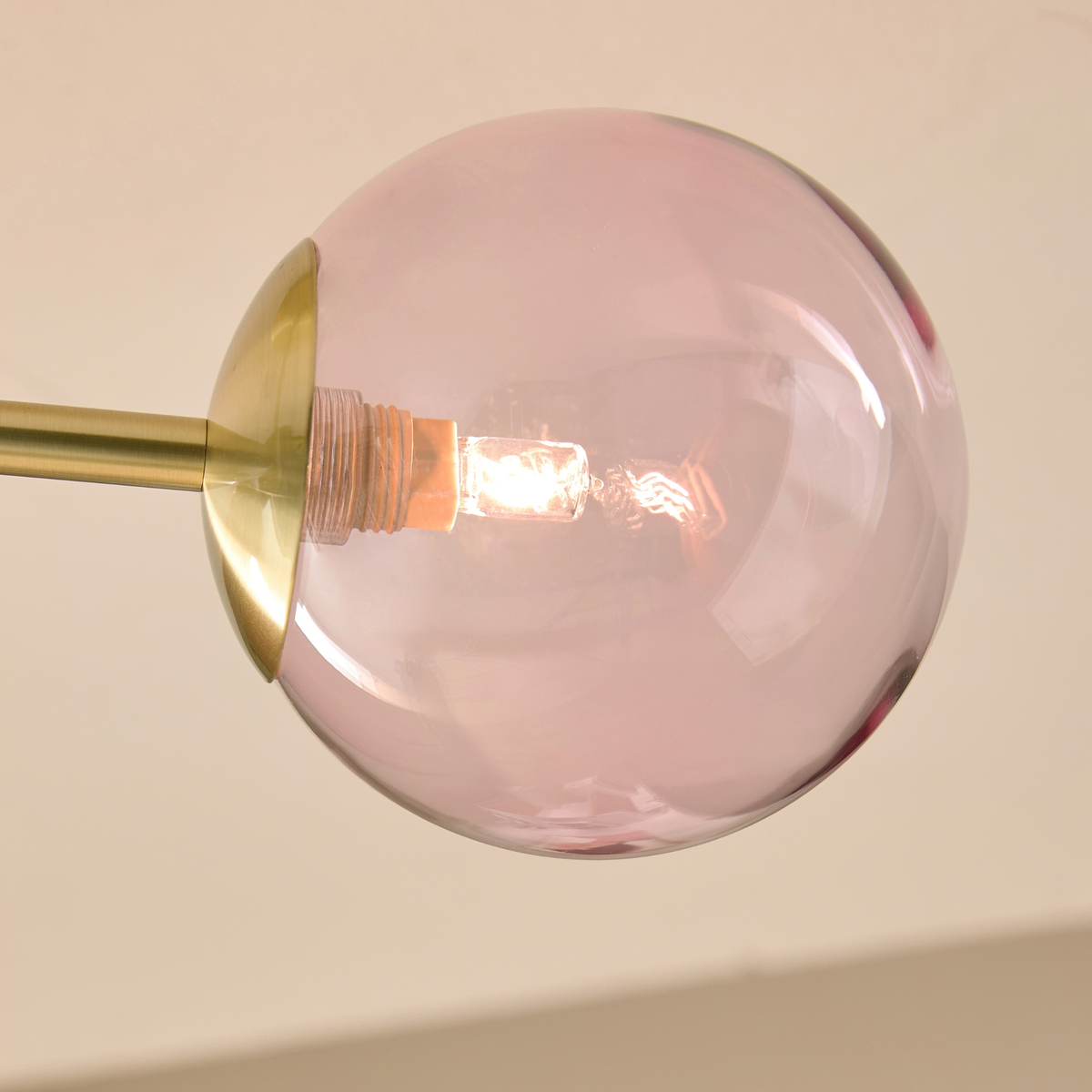 MADE.COM Globe 3 light flush ceiling light close up of a pink tinted glass globe and lit bulb
