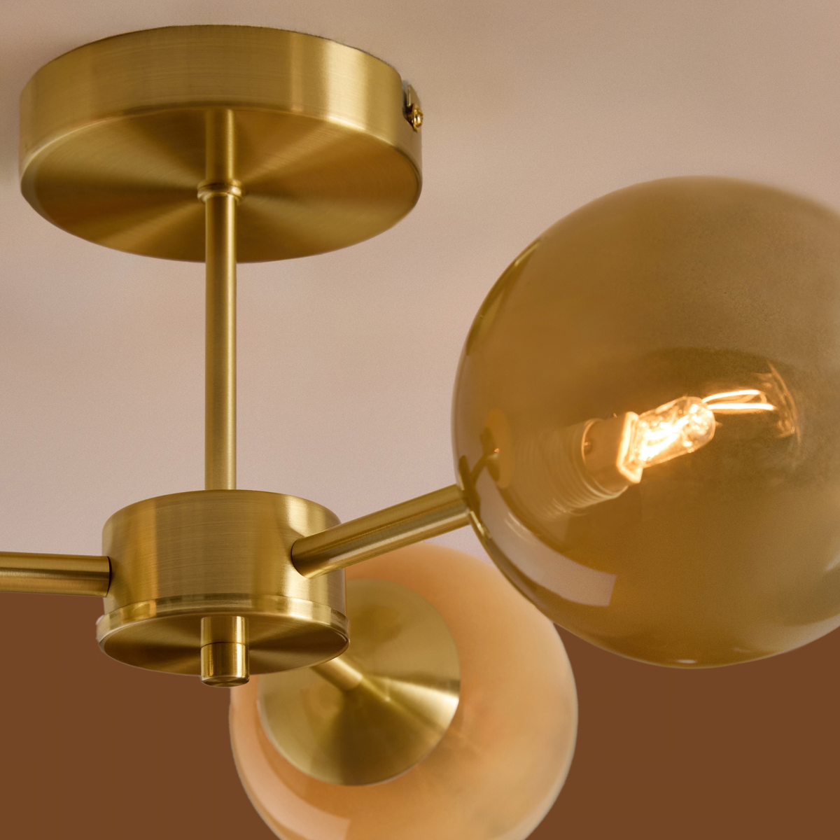 Close up of brushed brass ceiling plate and amber ombre globe on MADE.COM Globe 3 light ceiling light