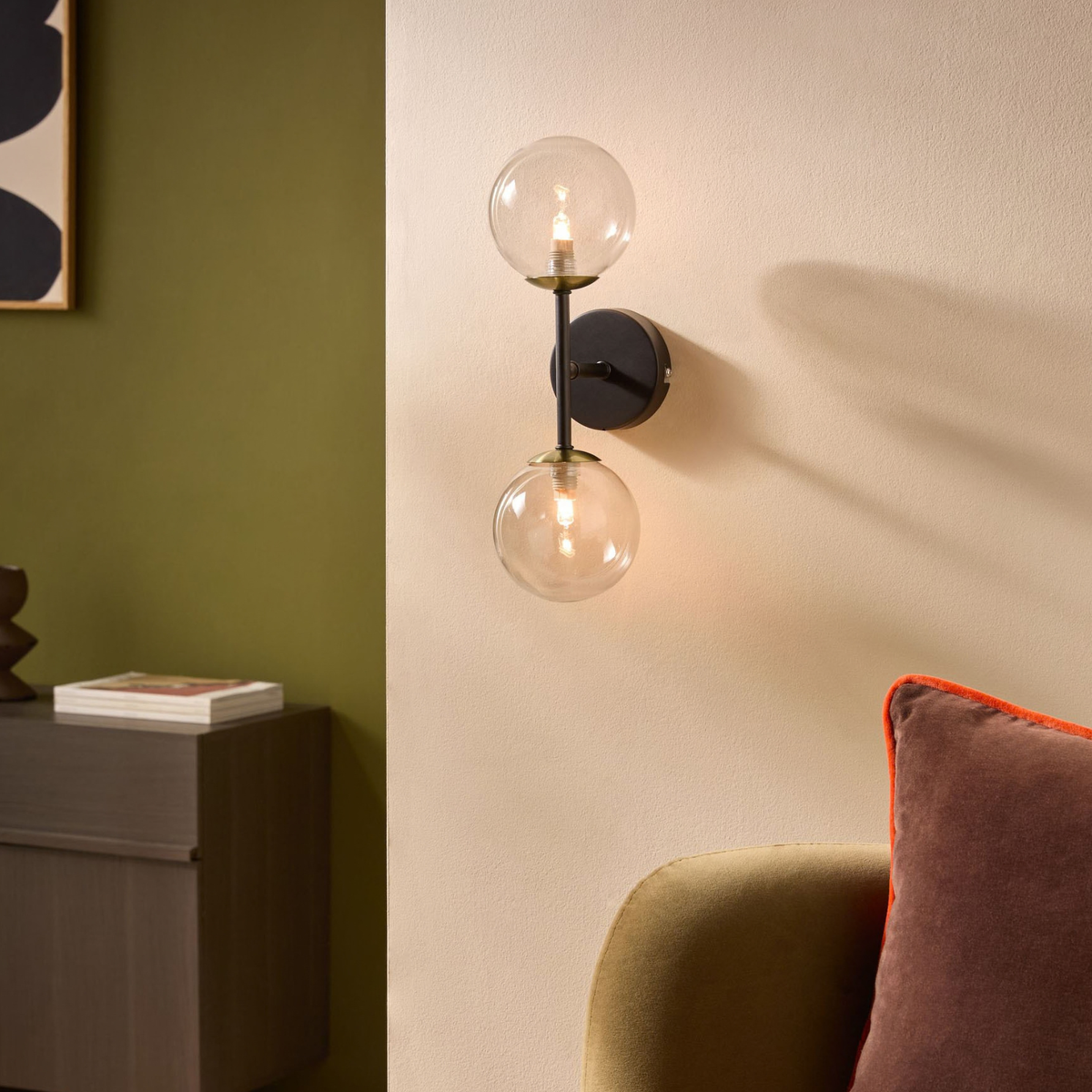 MADE.COM Globe wall light with two clear glass globes and matt black backplate above a green armchair