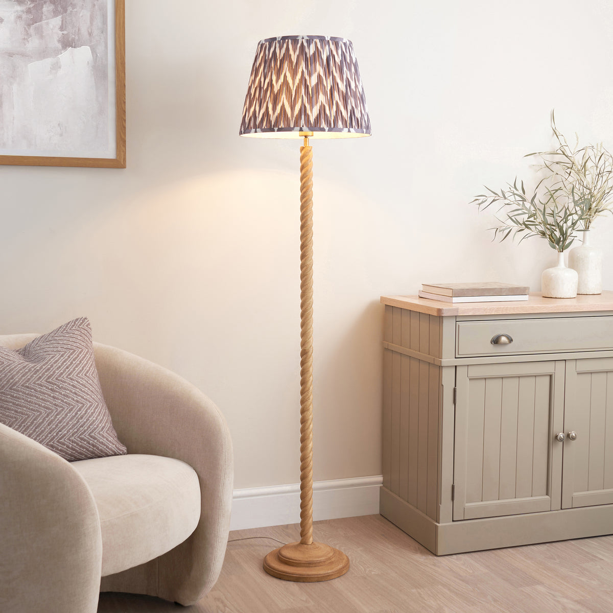 Endon Twist oak effect floor lamp lit in a living room beside a cream armchair, grey sideboard and framed artwork