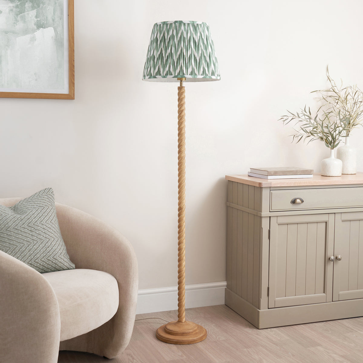 Endon Twist oak effect floor lamp with Cotswold green zigzag shade unlit in a neutral living room with armchair, sideboard and eucalyptus