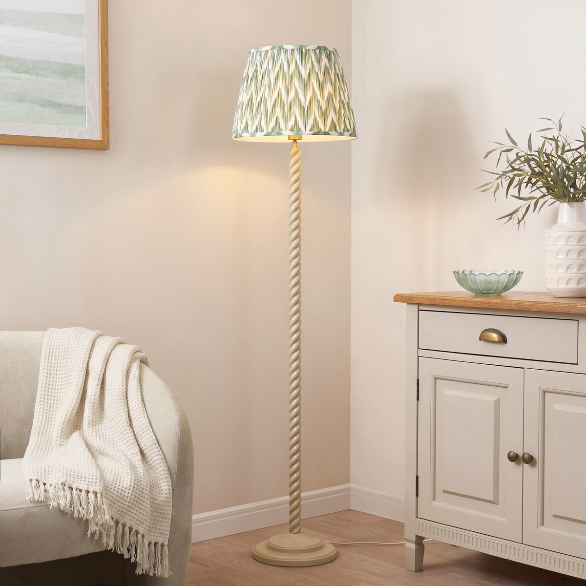 Endon Twist floor lamp lit in a cream room next to a grey sofa with a white throw, cream sideboard with eucalyptus vase and green glass bowl