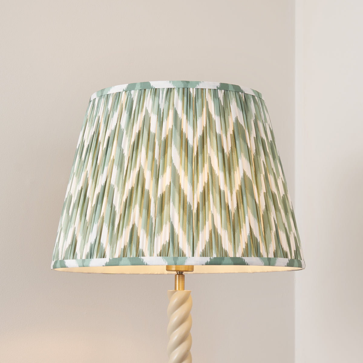 Close up of the Endon Twist floor lamp Cotswold green zigzag pleated shade lit, with the antique brass lamp holder and twisted stem below