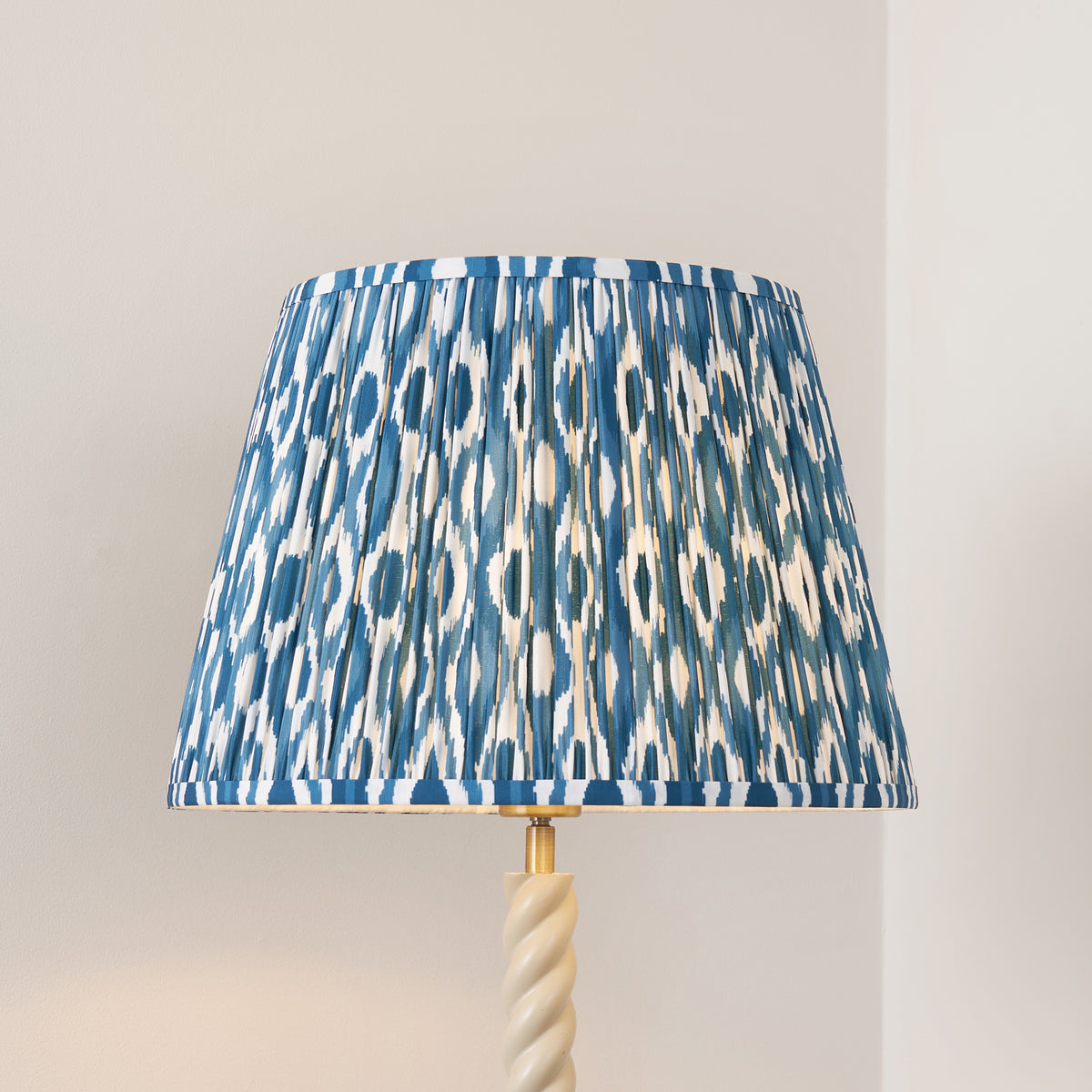 Close up of the pleated marlin blue ikat faux silk shade on the Endon Twist floor lamp's almond white twisted stem, unlit