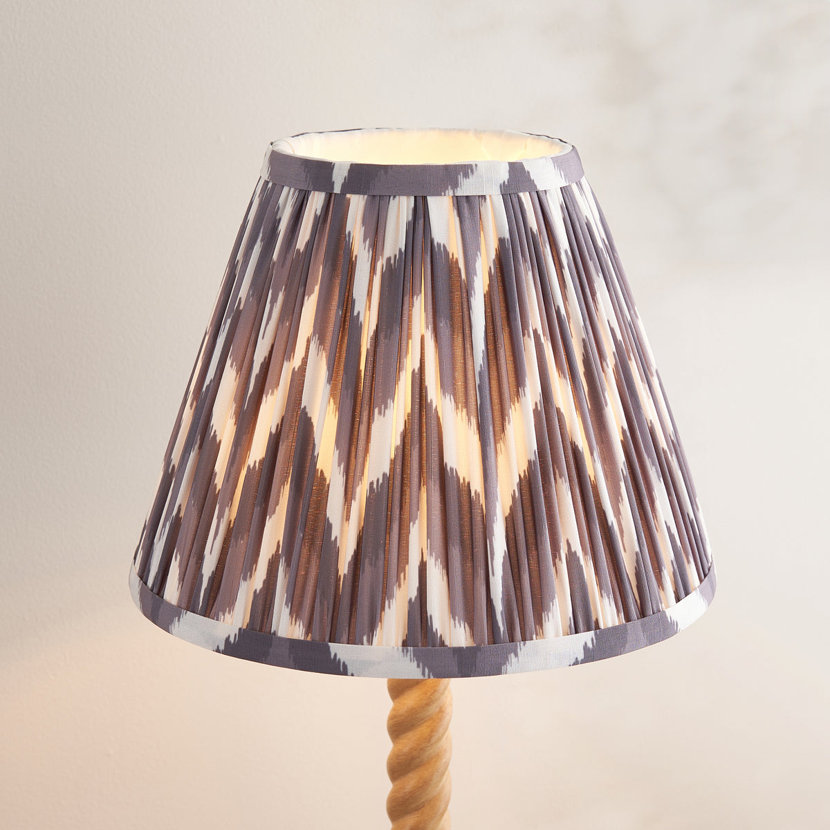 Close up of the lit pearl grey, brown and white zigzag pleated shade on the Endon Twist oak effect table lamp