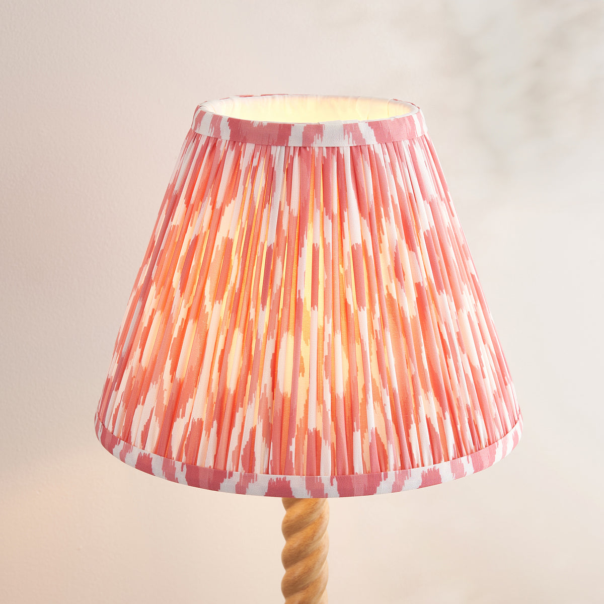 Close up of the lit coral pink ikat faux silk shade on the Endon Twist table lamp, showing the fine pleats and the top of the oak effect stem