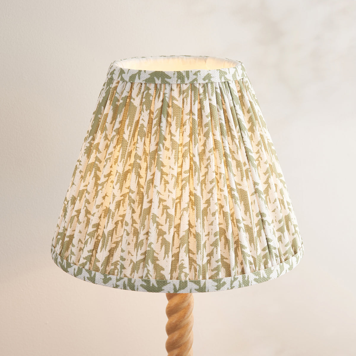 Close up of the lit 25cm Leaf shade on the Endon Twist table lamp, pleated faux linen with a herb garden green leaf print and taped edges