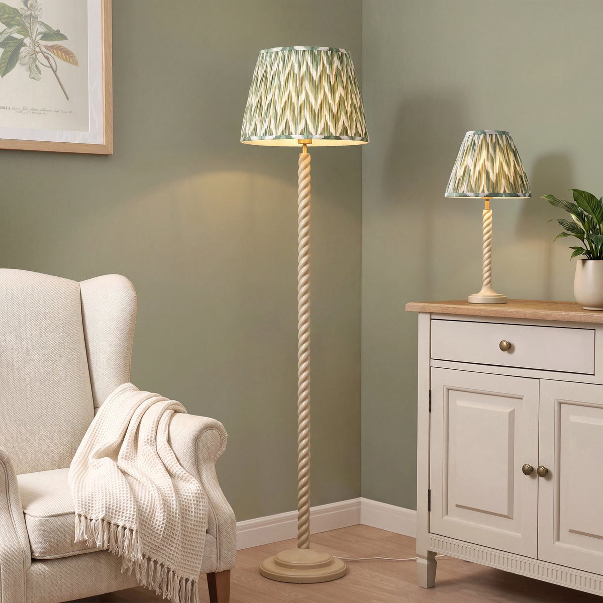 Endon Twist table lamp lit on a cream sideboard with the matching Twist floor lamp beside a cream armchair, green zigzag shades, sage green walls