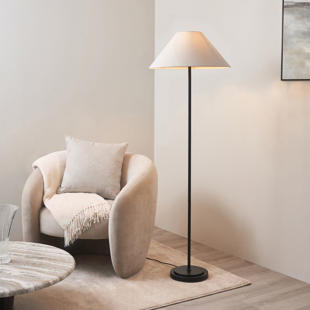 Endon Arlo matt black floor lamp with natural linen Avalon shade lit beside a cream curved armchair, rug and marble coffee table