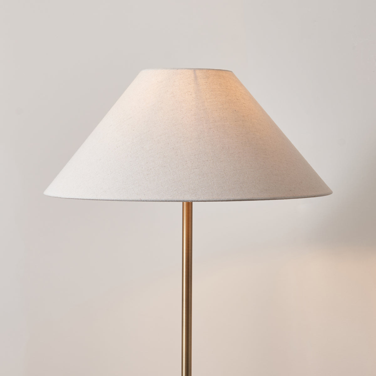 Close up of the Endon Avalon 52cm natural linen coolie shade on the antique brass Arlo floor lamp stem, lit against a plain wall